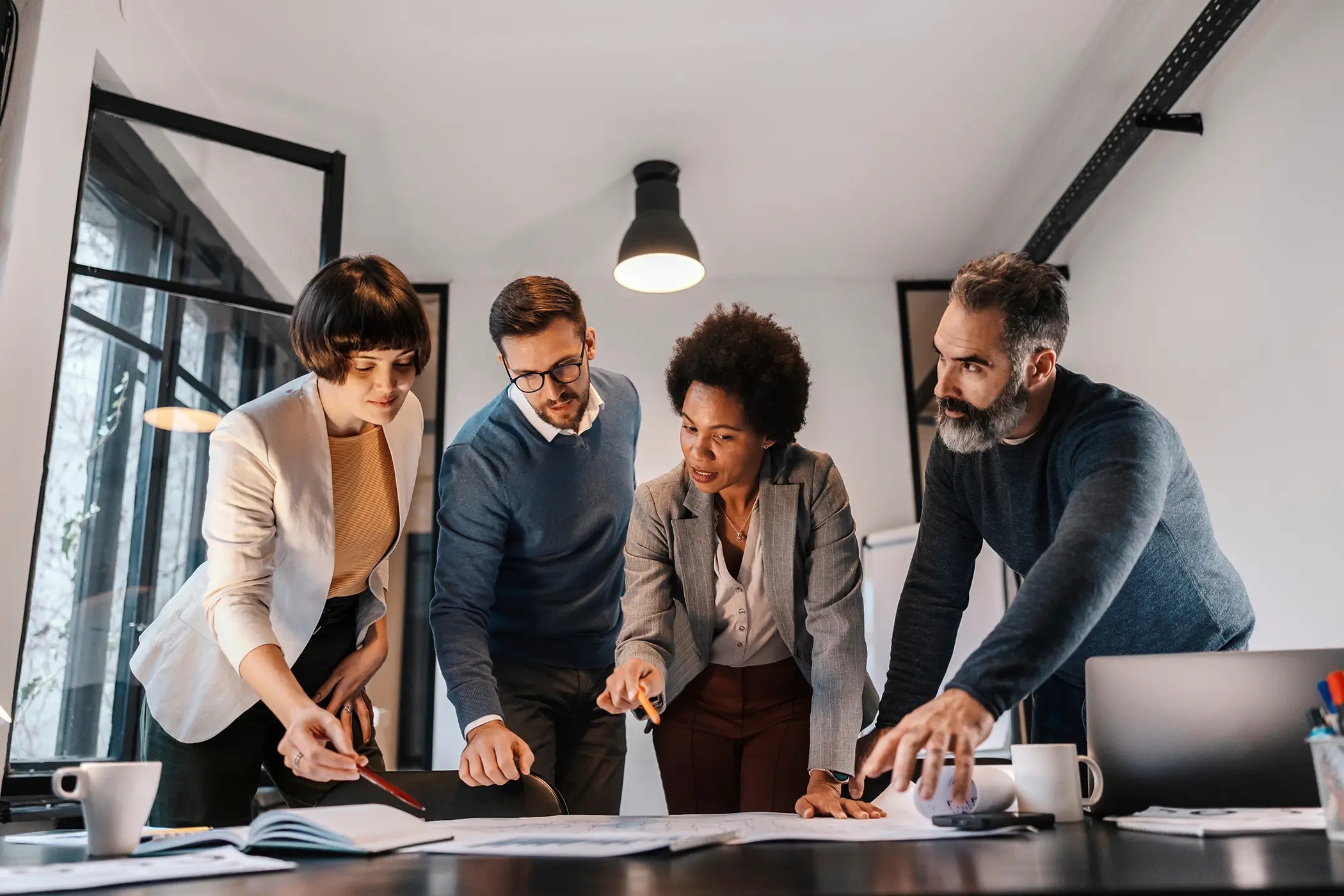 A interracial group of architects is pointing at the blueprints