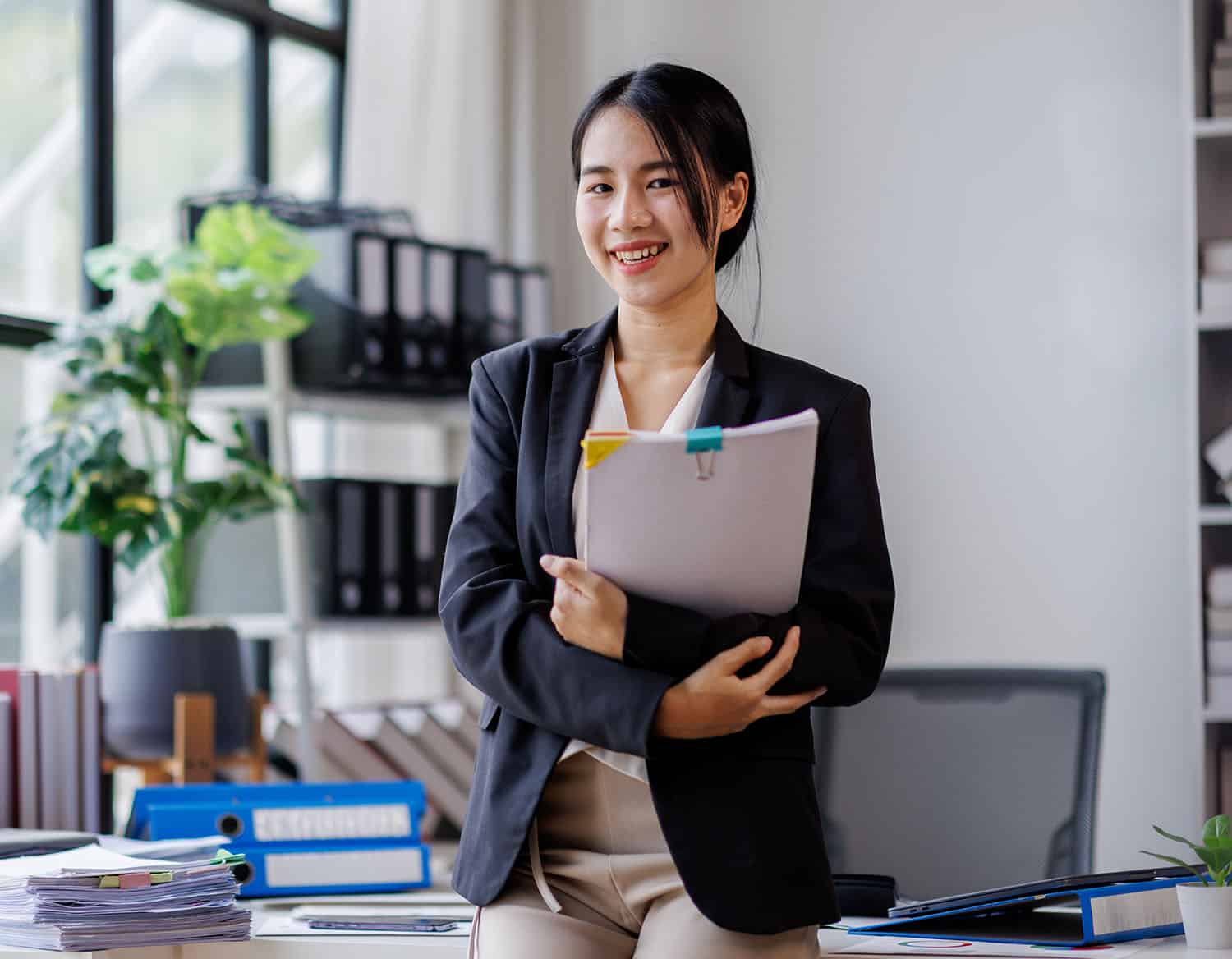 Office worker smiling holding folders in office.